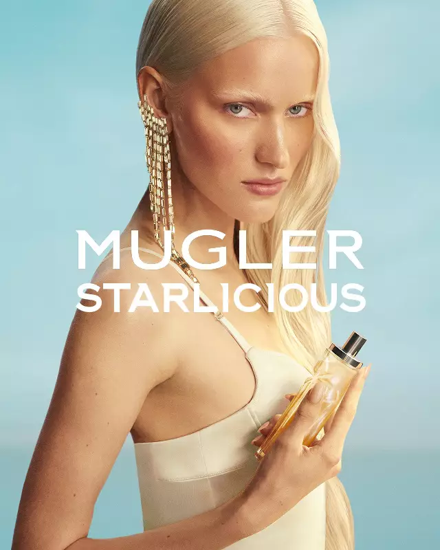 Bannière de la campagne Mugler Starlicious Les Eaux Gourmandes mettant en vedette une mannequin portant une robe jaune pâle et tenant le flacon Pineapple Musk, sur fond de ciel bleu doux.