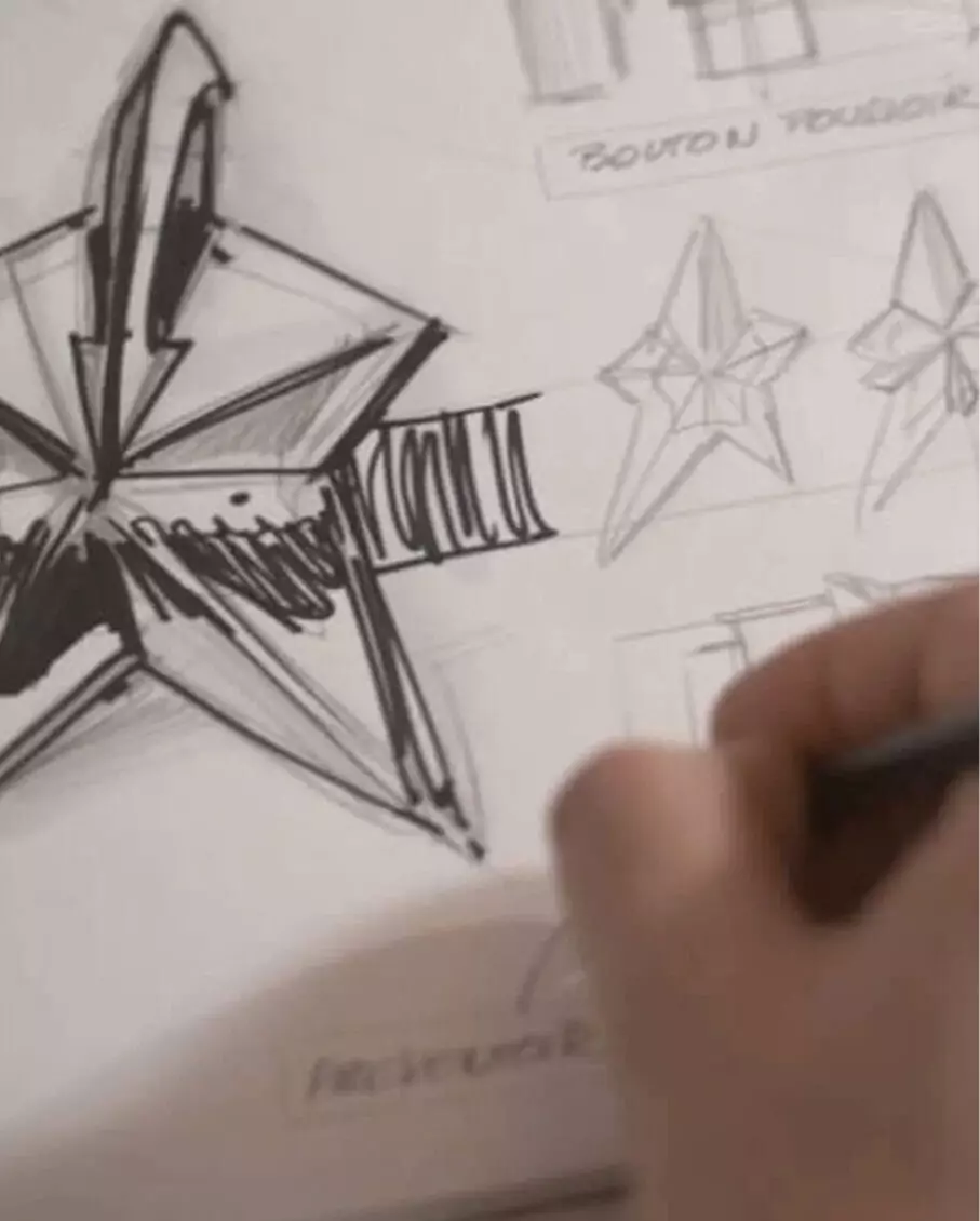 Designer hands sketching the architectural star design of a Mugler perfume bottle.