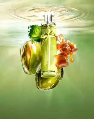 Une image de nature morte de Nouveau Starlicious Pistachio Praline mettant en vedette le flacon élancé entouré de ses ingrédients clés : une feuille de patchouli, des pistaches entières et des cubes de caramel fondant, sur fond d'eau ondulante d'un vert lumineux.