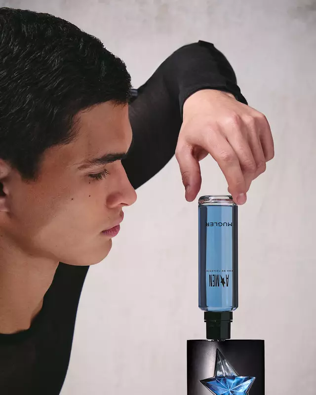 A hand refilling the black and blue star A*Men Eau de Toilette bottle using a blue refill bottle upside down.